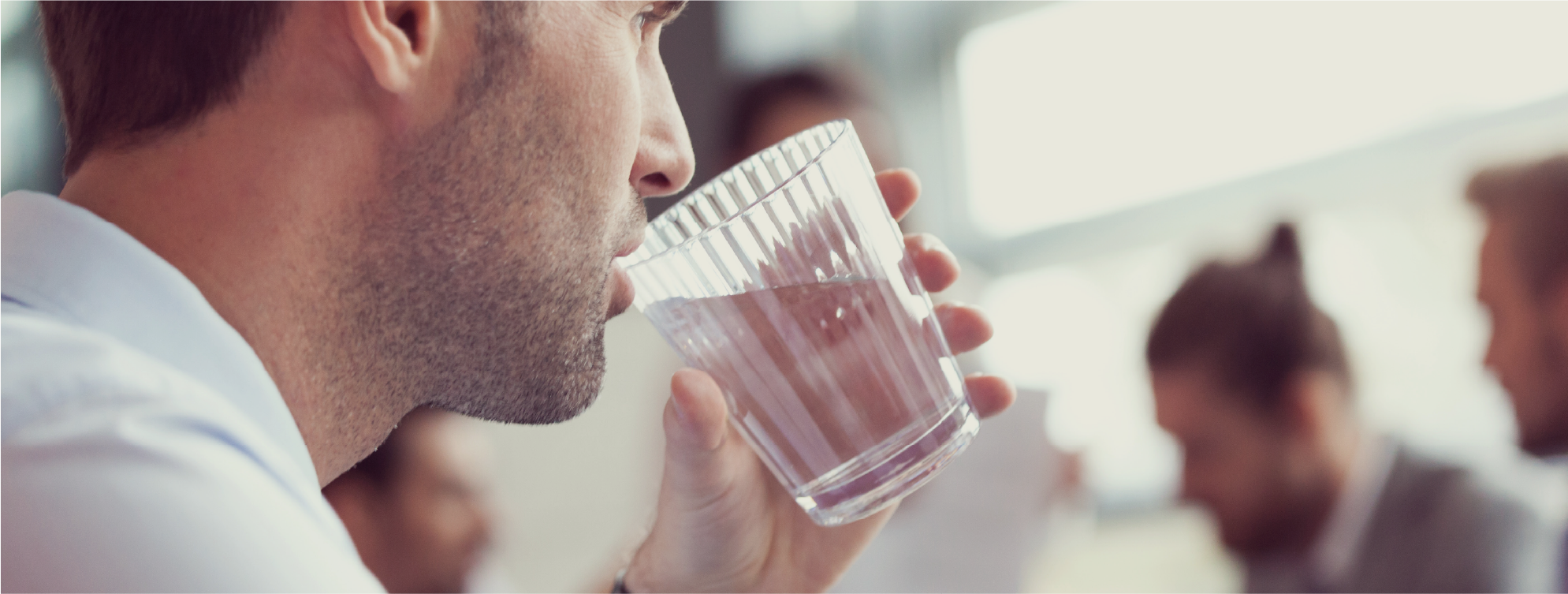 Close up of male in a meeting environment drinking from a clear glass of water.