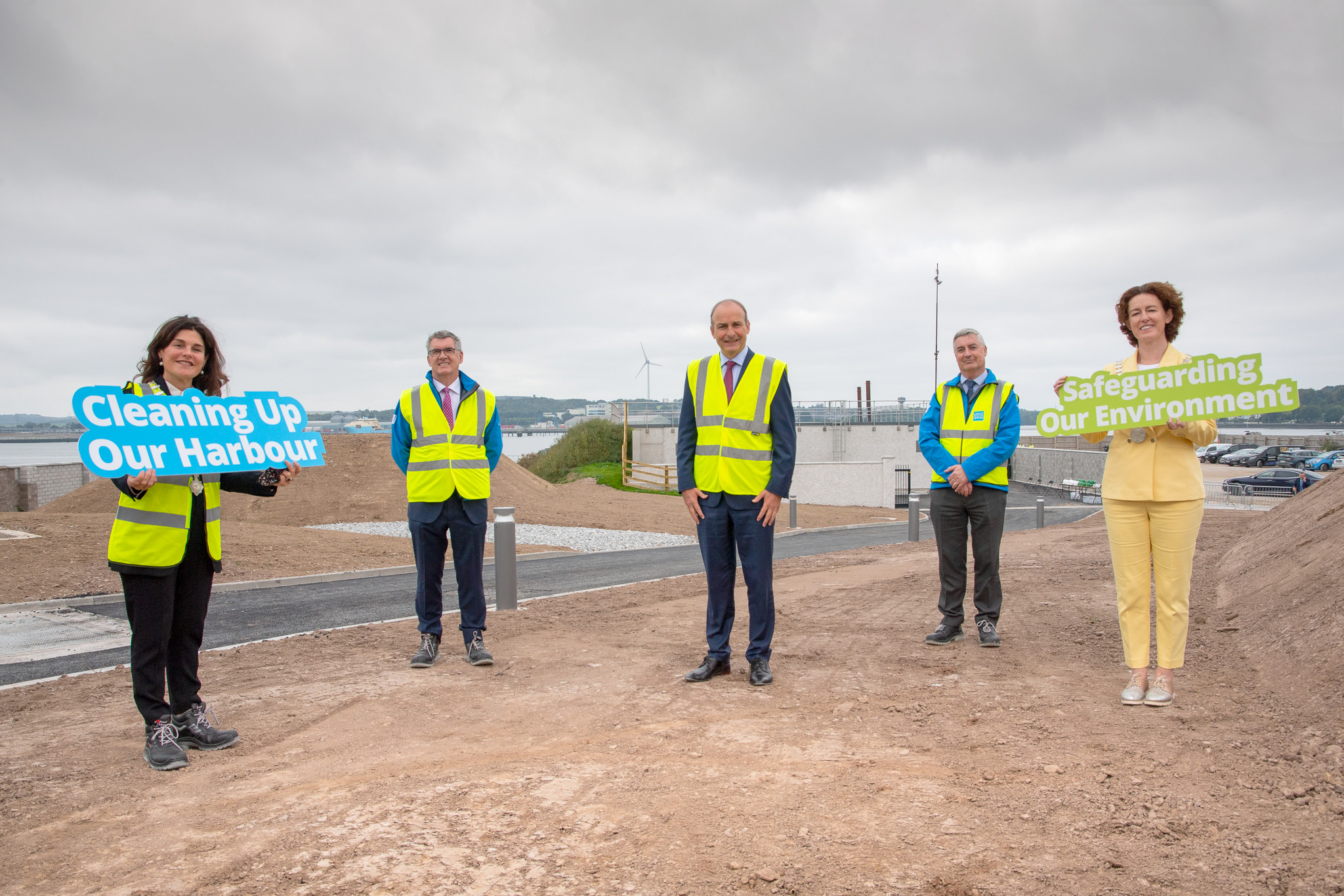 Micheal Martin standing with UÉ board members at a construction site holding signs for cleaning up the harbour and the environment