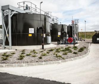 Four large black cylindrical tanks with pipes coming out of them