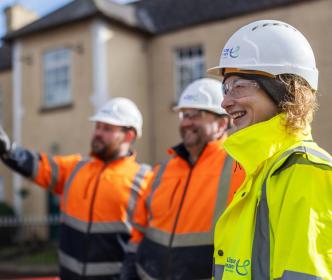 Two engineers wearing orange safety gear and another wearing a yellow high visibility jacket with a helmet