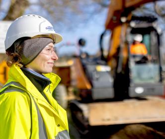 An engineer right beside a digger in works wearing safety gear