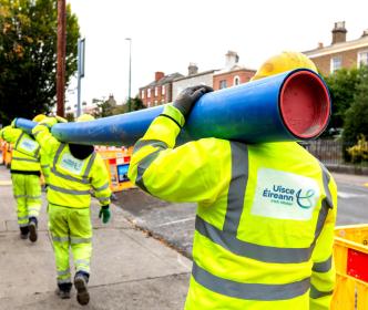 Three UÉ workers holding a blue pipe on their shoulders